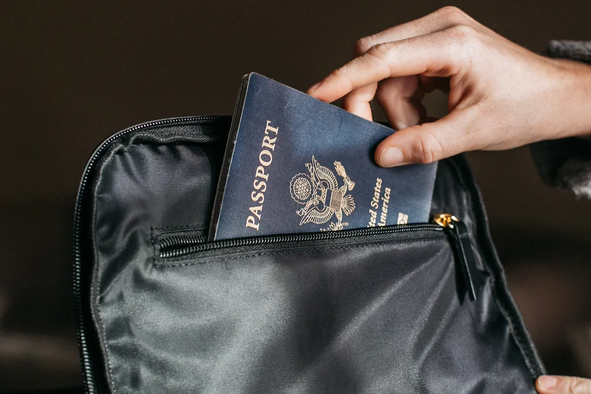 A closed passport being placed in a travel bag